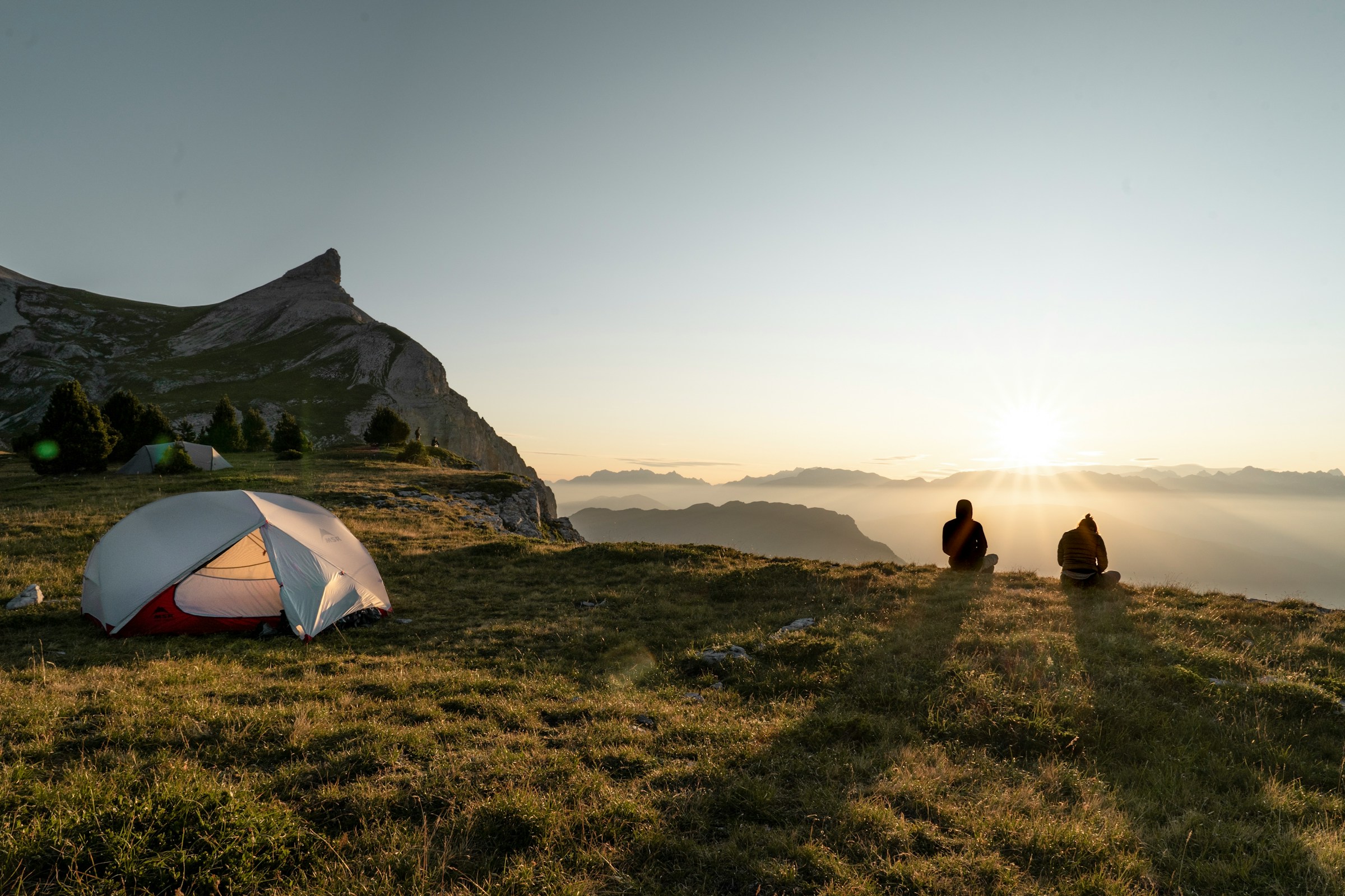 Two people overlooking a wide mountain landscape at sunrise